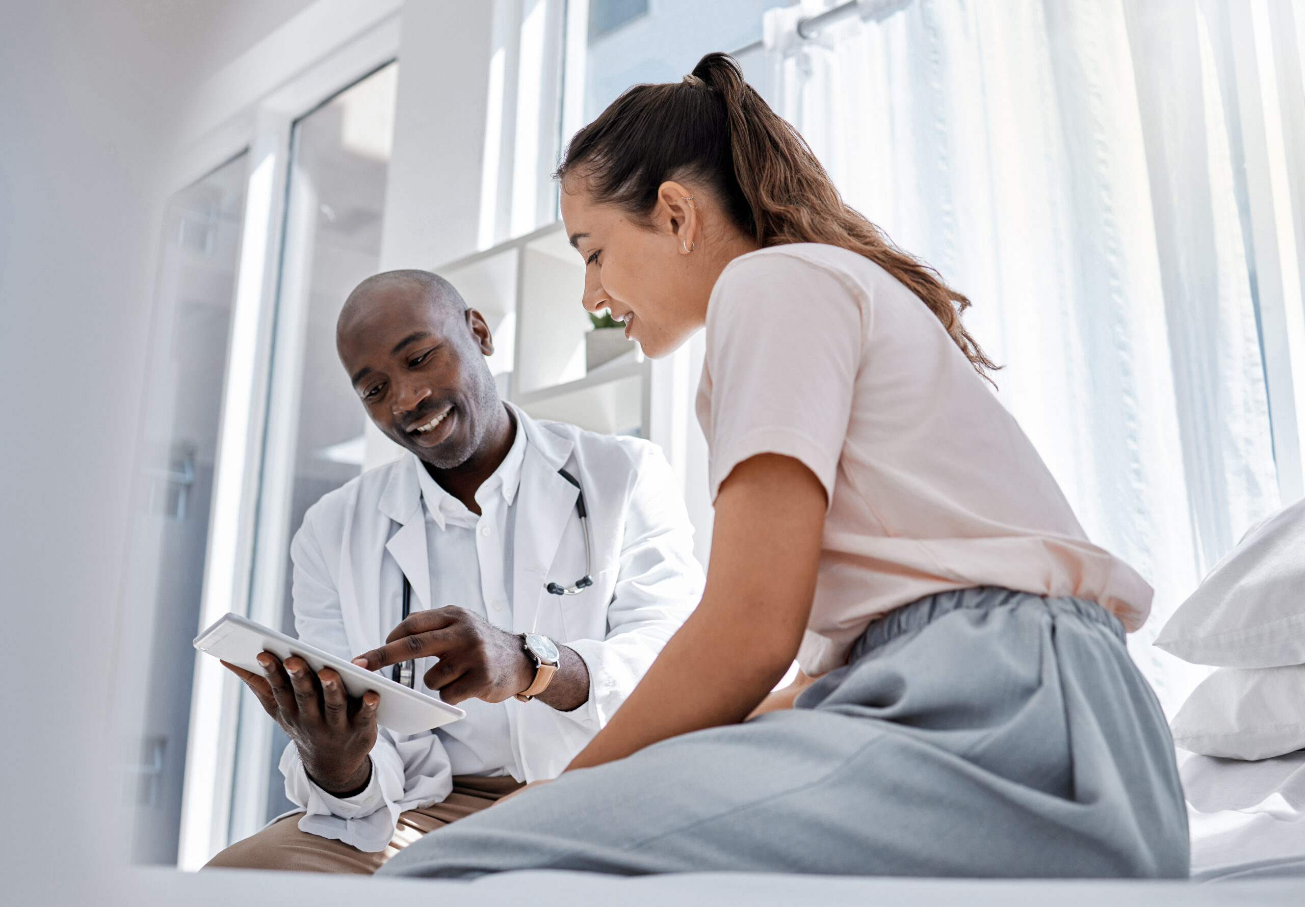 Doctor appointment or healthcare professional consulting a patient and showing her online medical results on a tablet. Medical worker or GP talking to a woman in a hospital or clinic